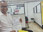 Juliano dos Santos Vicente celebra a oportunidade conquistada na Super Quarta da Funsat, segurando o documento que comprova sua participação no processo seletivo para operador de caixa.
