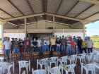 Um grupo de aproximadamente 40 pessoas posa para foto em uma estrutura coberta, semelhante a um barracão rural