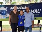 Lucas Jamal ao lado dos pais, comemorando a medalha de ouro conquistada no World Jiu-Jitsu Championship, com faixa de homenagem ao fundo.