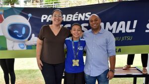 Lucas Jamal ao lado dos pais, comemorando a medalha de ouro conquistada no World Jiu-Jitsu Championship, com faixa de homenagem ao fundo.