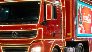 Caminhões iluminados da Caravana de Natal desfilando à noite, com público assistindo nas calçadas.