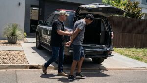 Homem é preso por policial e conduzido algemado até viatura em frente a residência durante operação policial.