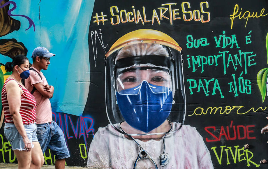 Pedestres caminham na frente de grafite em alusão ao surto do novo coronavírus na zona norte de São Paulo