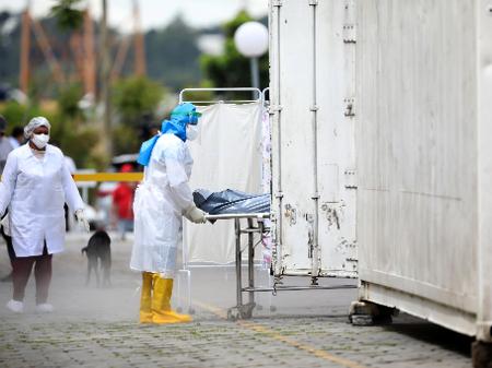 Um profissional de saúde transportando o corpo de uma pessoa para um caminhão refrigerado