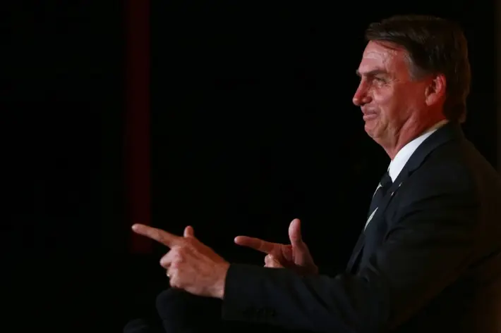 O presidente Jair Bolsonaro faz gesto para simular uma arma durante evento.
