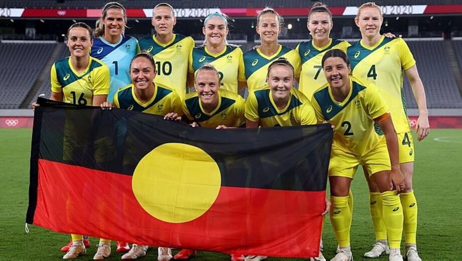 Jogadoras australianas posam com bandeira em referência aos povos indígenas