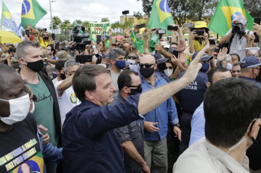 Sem máscara, o presidente Jair Bolsonaro, cercado por um cordão de isolamento de seguranças, cumprimenta simpatizantes na frente do Palácio do Planalto.
