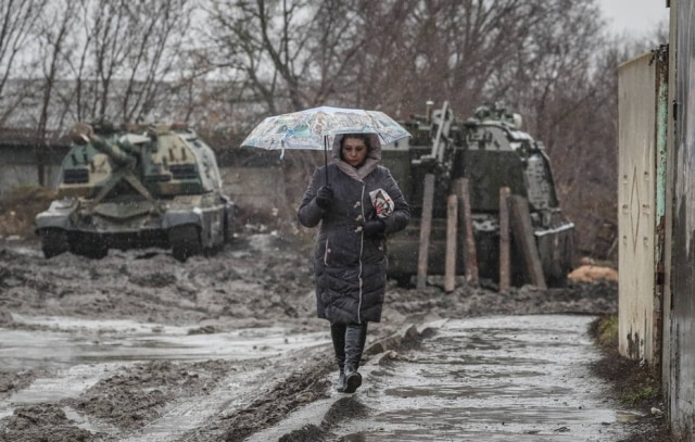 Mulher caminha na frente de veículos blindados russos na estação ferroviária na região de Rostov, Rússia. Personalidades lamentam a ofensiva Russa contra a Ucrânia.