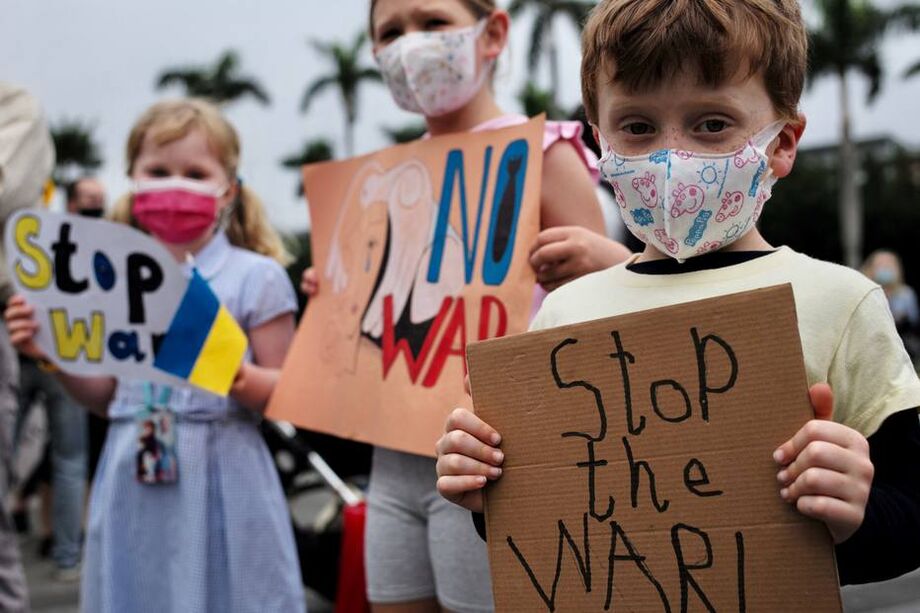 Três crianças eslavas exibem cartazes durante um protesto contra a invasão militar da Ucrânia pela Rússia.