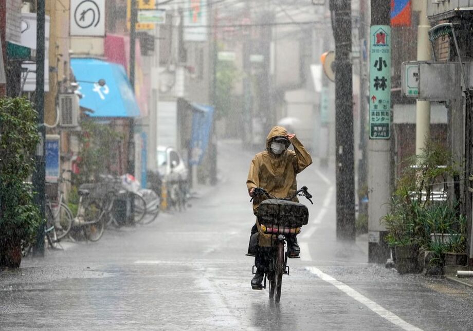 Mulher pedala sob chuva pesada aem Tóquio, no Japão, nesta quarta-feira, 20
