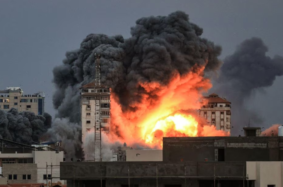 Pessoas veem prédio ser bombardeado na Faixa de Gaza.