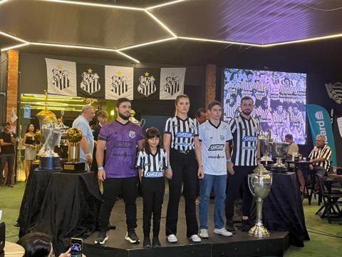 Isabela, vestindo o uniforme infantil, Natália, com a listrada baby look, Miguel, exibindo a camiseta Branca 2º uniforme, Genaro, com a camisa de goleiro, e Breno, ostentando a listrada principal