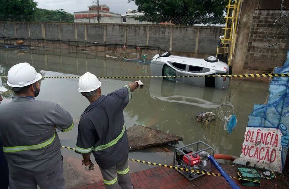 Homens observam um carro na água e a destruição causada por fortes chuvas que atingiram o Rio de Janeiro