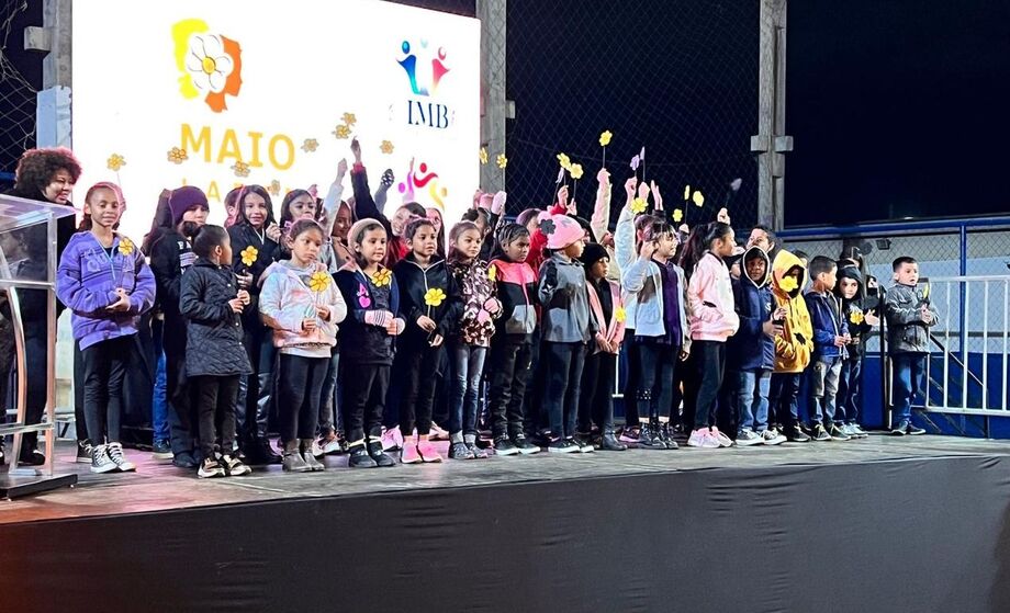 um grupo de crianças atendidas pela OSC, em cima do palco, durante apresentação cultural;
