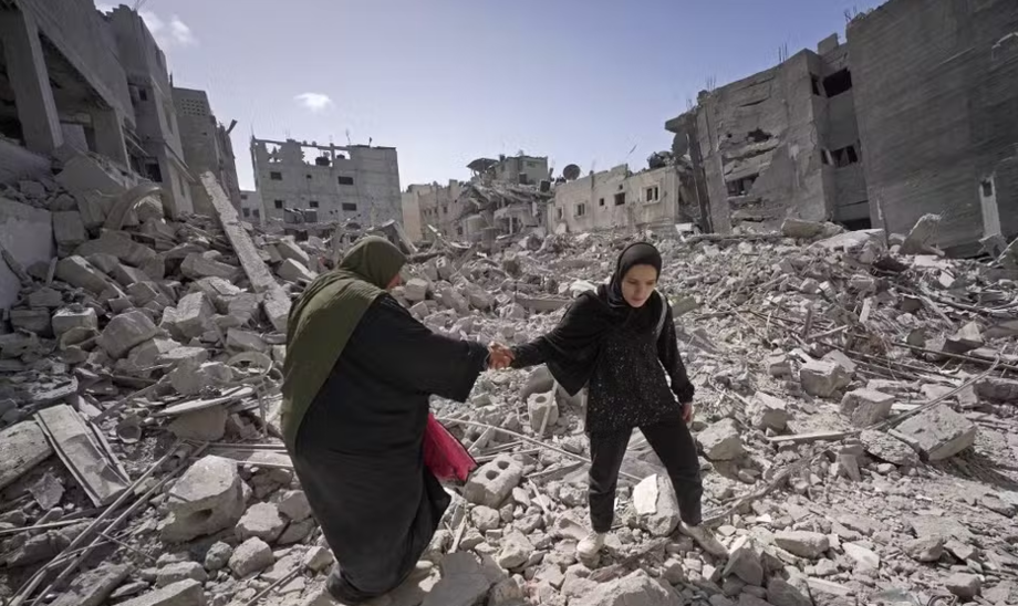 Palestinos caminham por escombros em Khan Younis, no sul de Gaza, após bombardeio israelense, em março deste ano