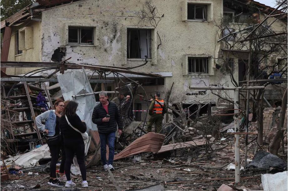 Pessoas aguardam enquanto as forças de segurança israelenses inspecionam a vizinhança de uma casa danificada em um local atingido por foguetes disparados do Líbano na vila de Rinatya, no centro de Israel, em 24 de novembro de 2024