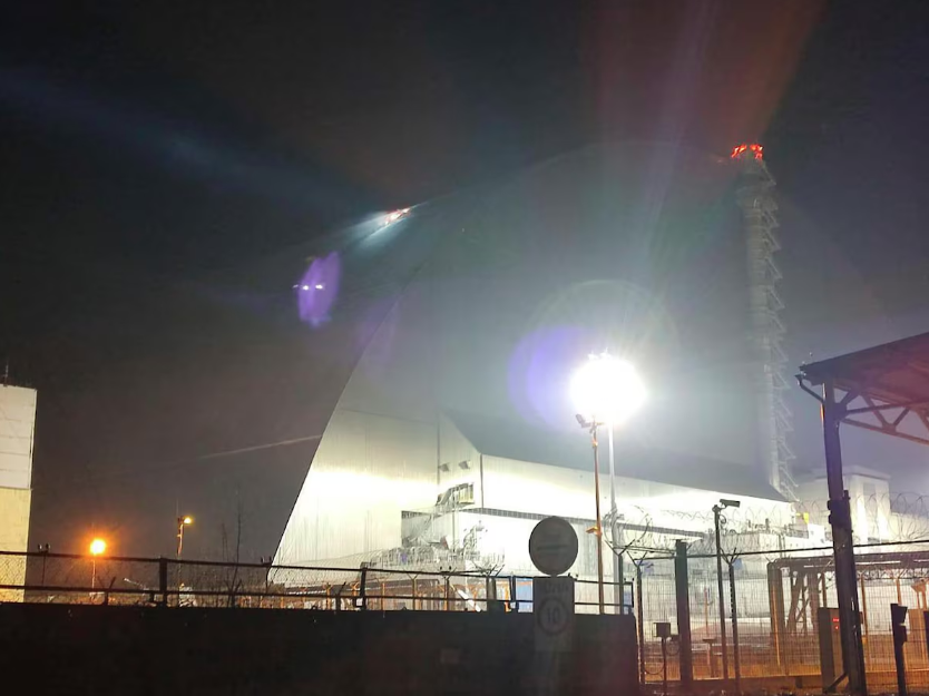 Um holofote ilumina um buraco no telhado de um sarcófago danificado, que cobre o destruído 4º reator da usina nuclear de Chernobyl, após um ataque de drone russo em Chernobyl, Ucrânia, na sexta-feira, 14 de fevereiro de 2025.