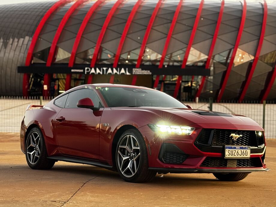 Mustang GT vermelho posicionado para testes em frente ao Bioparque Pantanal, ícone da arquitetura local.