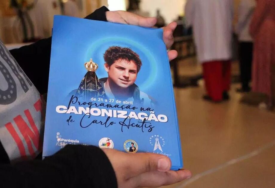 Fiéis seguram panfleto da programação da canonização de Carlo Acutis, adiada após a morte do Papa Francisco.