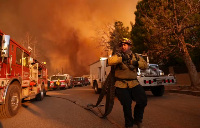 Bombeiro carrega mangueiras diante de incêndio em Palisades, em Los Angeles, nos EUA, em 11 de janeiro de 2025.