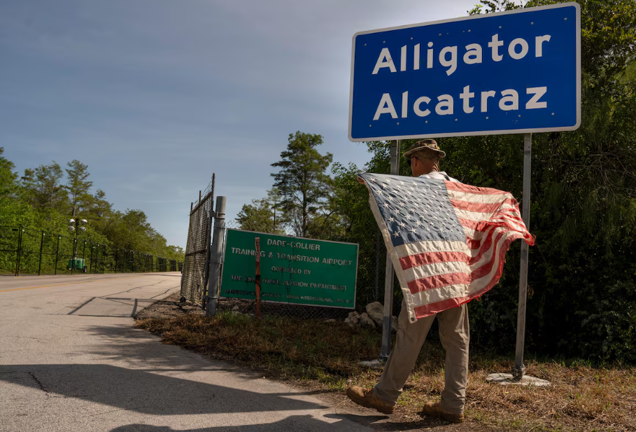 Imagem mostra um homem com a bandeira dos EUA na entrada da 'Alcatraz dos Jacarés', um centro de detenção de imigrantes da Flórida. Estado reivindica autonomia para deter migrantes sem status legal