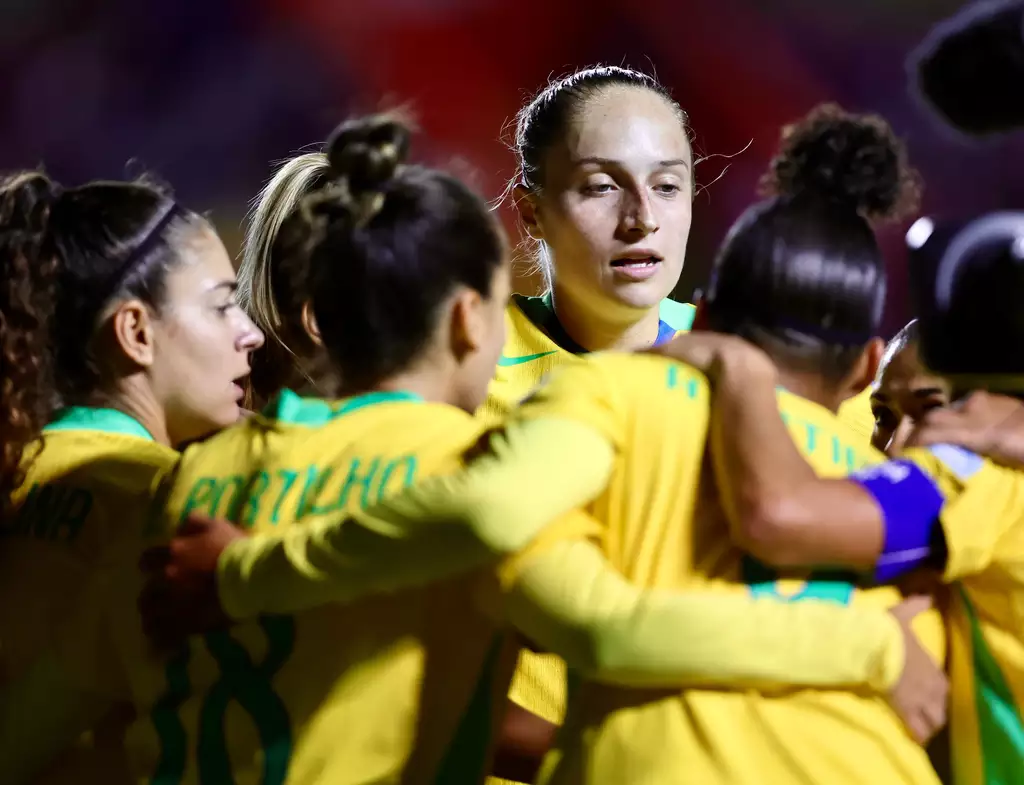 Jogadoras comemoram vitória com abraço em grupo no gramado.