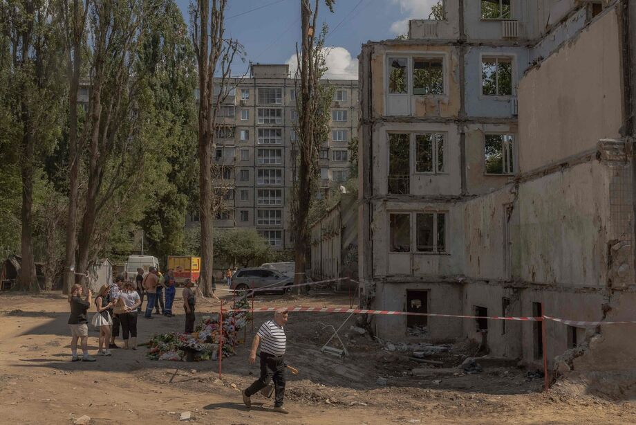 Pessoas se reúnem ao lado de flores, brinquedos infantis e retratos colocados em memória das vítimas no local de um prédio residencial de nove andares destruído após um recente ataque com mísseis russos em Kiev, em 5 de agosto de 2025
