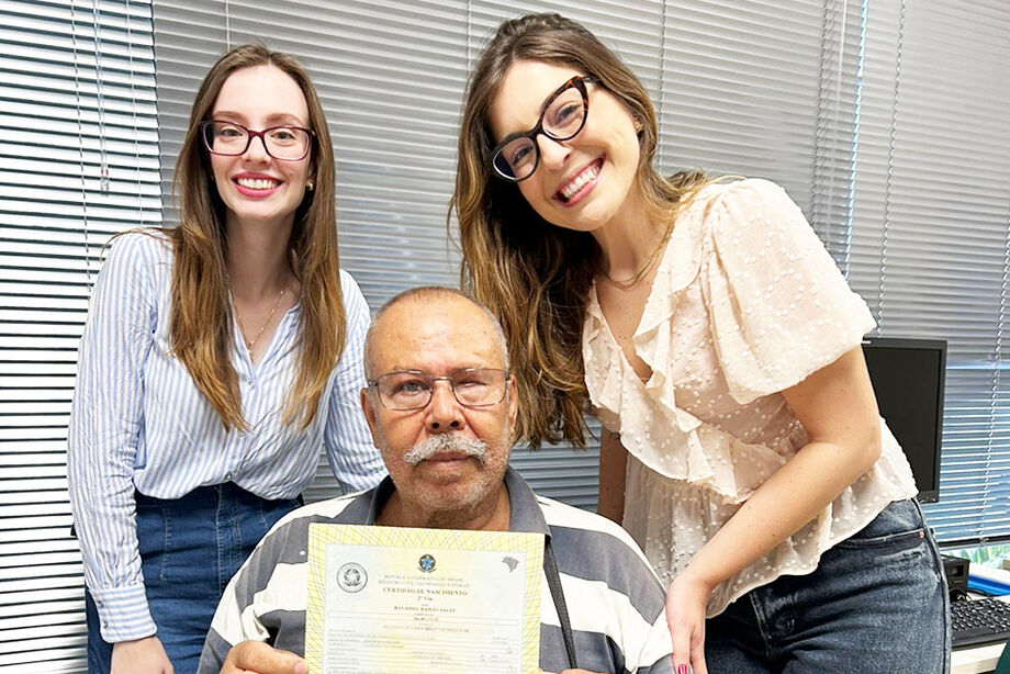 Ravadiel Ramão Sales recebe certidão de nascimento das mãos de Stephany Fonseca (à dir.), defensora, e Amanda Mehret, assessora jurídica