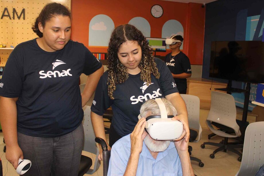 Alunos do curso de serviços administrativos do Senac MS ajudam idoso a interagir com a tecnologia em ação de inclusão digital.