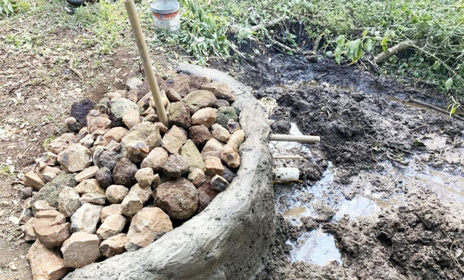 Técnicos trabalhando na proteção de uma nascente cercada por vegetação, com a estrutura de solo-cimento visível.