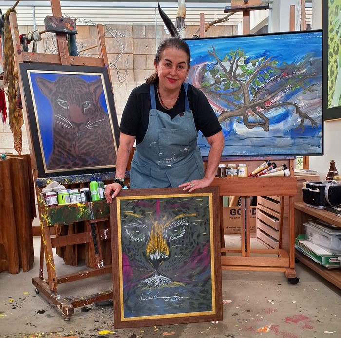 A artista plástica Lúcia Martins Coelho Barbosa, com três de suas obras, duas delas com onças, sua marca registrada