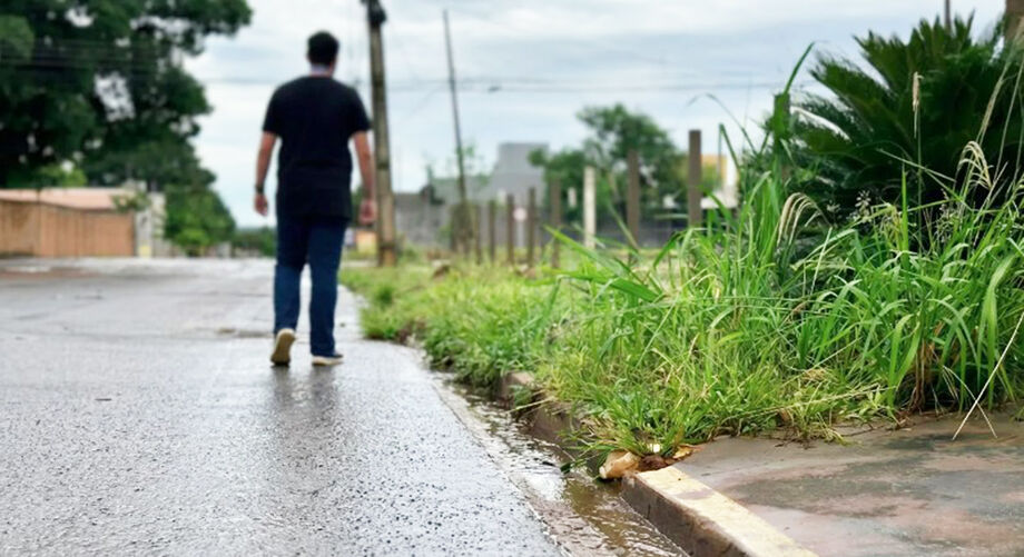 Pedestre caminha pela rua diante da ausência de calçadas adequadas, realidade comum em bairros de Campo Grande.
