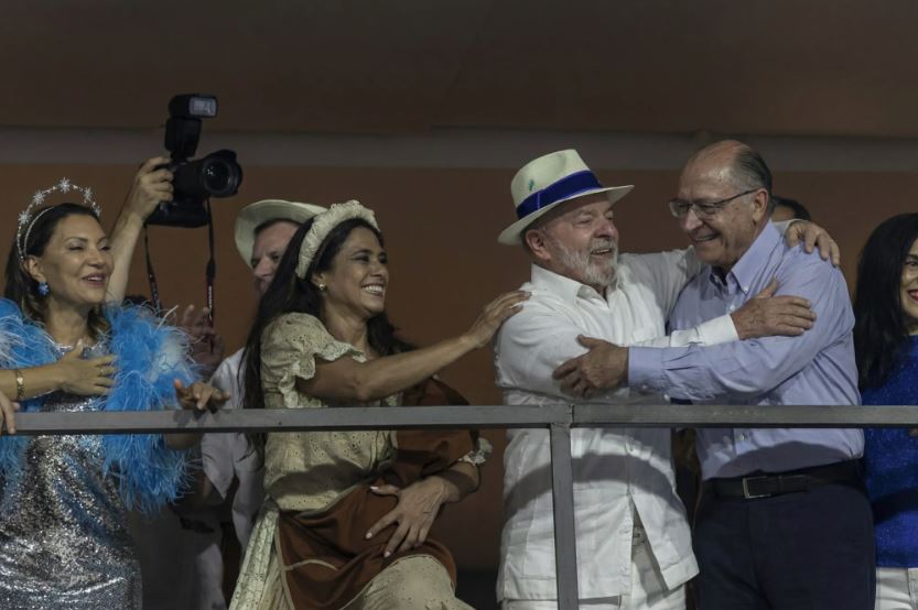 Presidente Lula acompanha desfile na Sapucaí enquanto grupo próximo faz gesto de oposição.