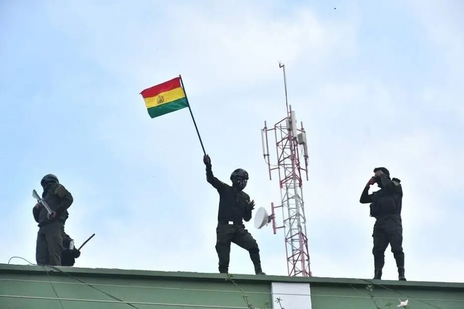 Policiais bolivianos com bandeira do país em uma unidade da polícia de Cochabamba