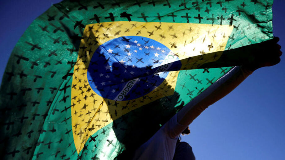 Ativista segura uma bandeira brasileira pintada com cruzes simbolizando as mortes por coronavírus, e