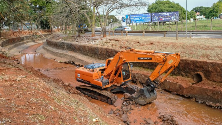 Nesta quarta-feira (12) uma retroescavadeira, da empreiteira responsável pela obra, iniciou a reconstrução do piso de pedra, revestido com concreto, feito no canal do córrego para evitar que a correnteza bata no barranco e derrube o muro de gabião