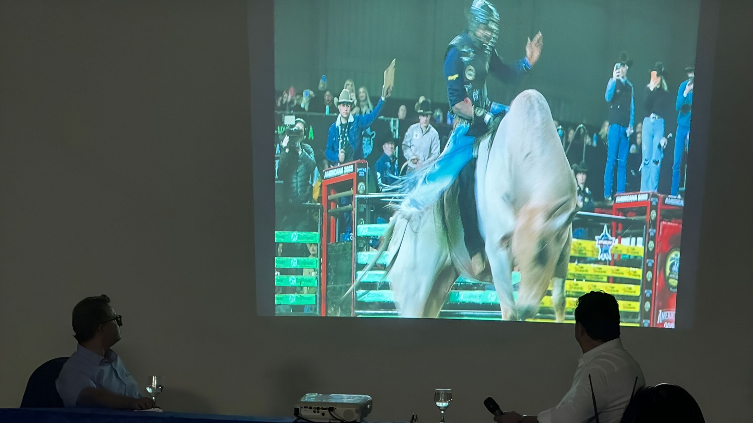 Guilherme Bumlai, presidente da ACRISSUL, e Paulo Mattos, presidente da Nelore MS, assistem à projeção de uma competição de rodeio durante o lançamento da Expogenética MS, que celebra as tradições locais e contribui para o turismo e comércio na região - (
