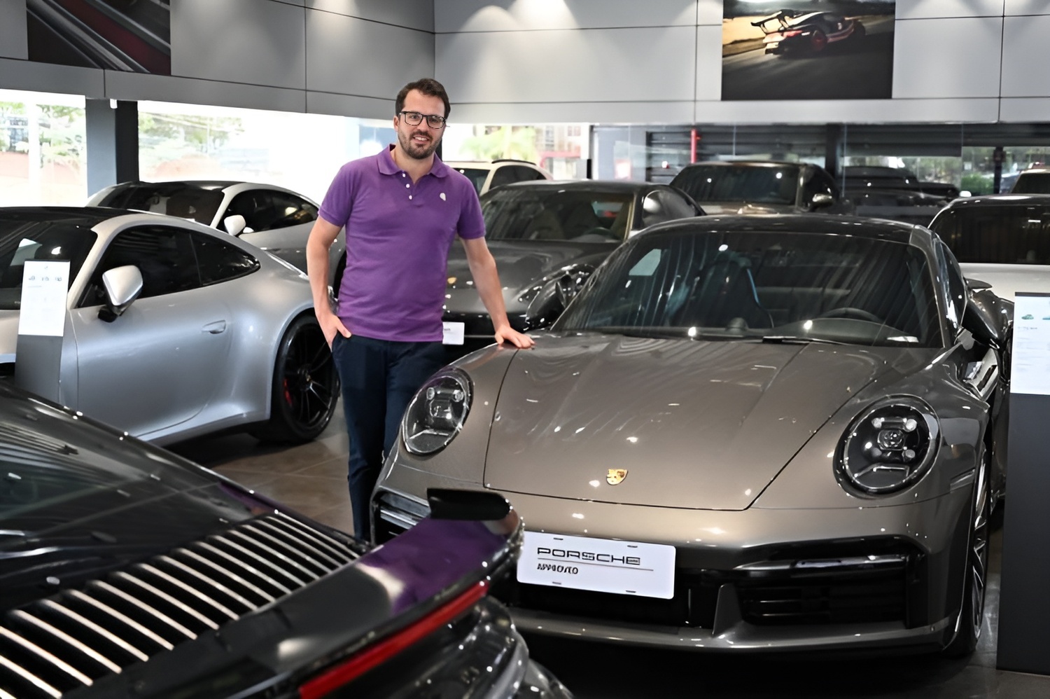 Clemente de Faria Jr., CEO do Grupo Bamaq, no elegante showroom da Porsche, destacando o prestígio e a sofisticação da marca, ao lado de um icônico Porsche 911.