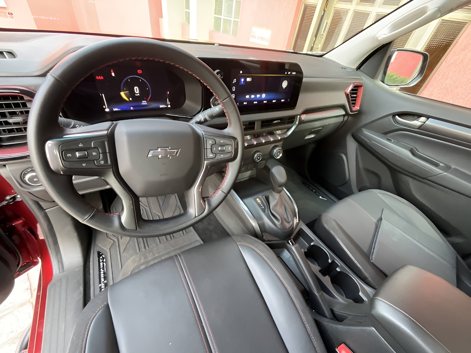 No interior da S10 Z71, o volante com acabamento em couro e as costuras vermelhas tentam dar um toque esportivo. A tela central amplia as funcionalidades, mas o ar-condicionado ainda é manual.