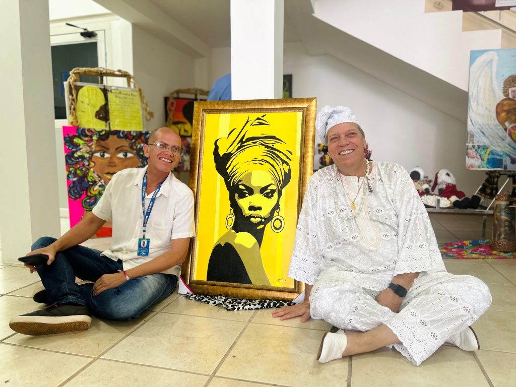 Ao lado da obra de Juan Ângelo, o técnico da Subsecretaria de Políticas Públicas para Promoção da Igualdade Racial, Roberto Cardoso e o presidente do Cedine, Pedro Gaeta. (Foto: Matheus Carvalho/SEC)