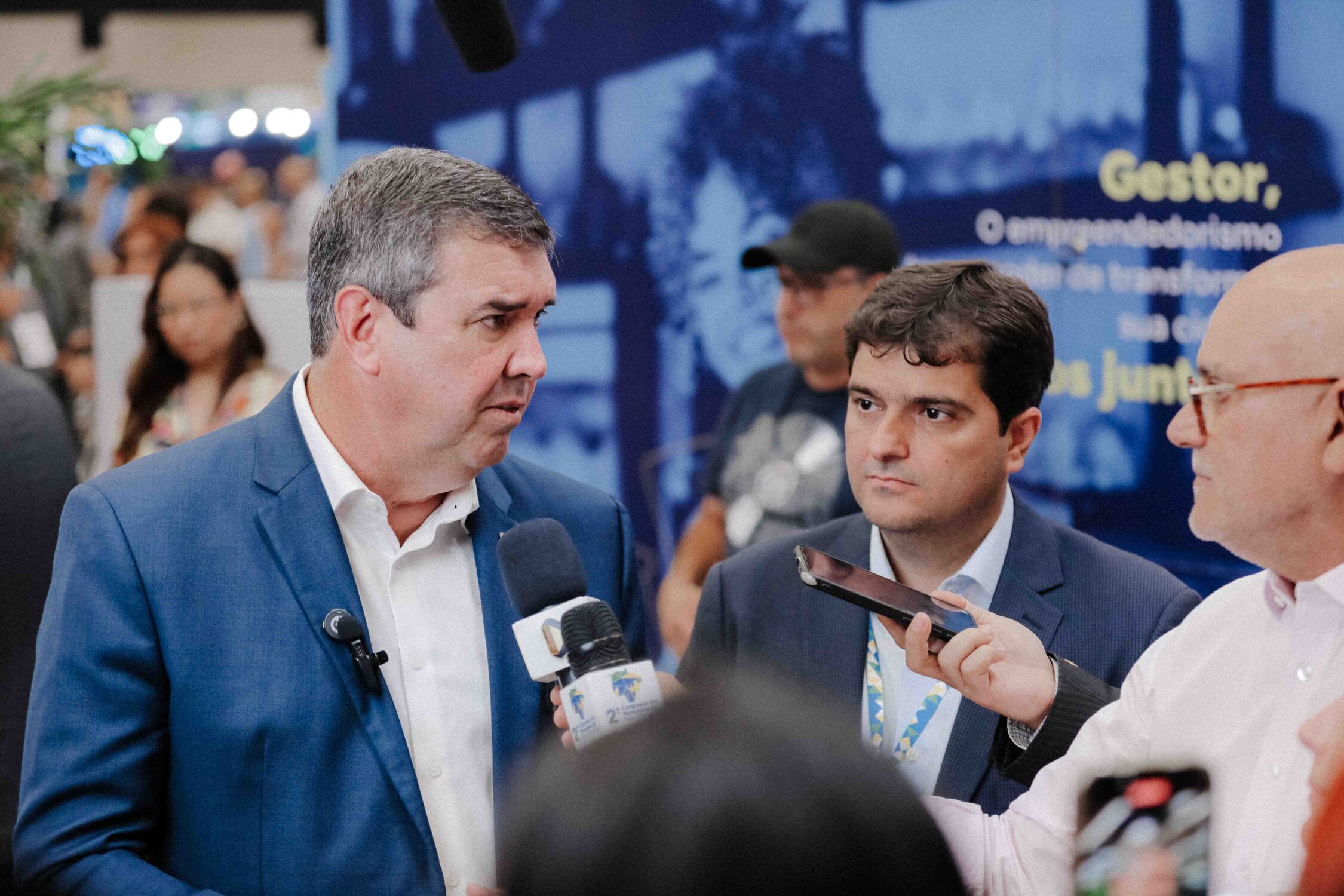 Eduardo Riedel, governador de Mato Grosso do Sul, fala com a imprensa durante o Congresso dos Municípios, ao lado de Valdir Júnior, presidente da Assomasul. Riedel destacou a importância das parcerias entre o governo estadual e os municípios para enfrenta