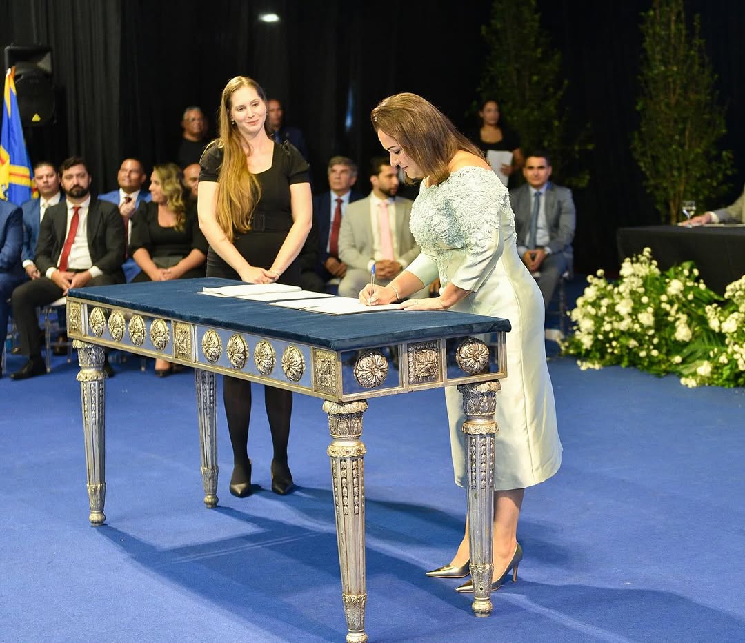 Adriane Lopes assina o termo de posse como prefeita de Campo Grande, oficializando seu mandato. Ao fundo, autoridades e convidados acompanham o momento histórico que marca uma nova fase para a capital sul-mato-grossense.