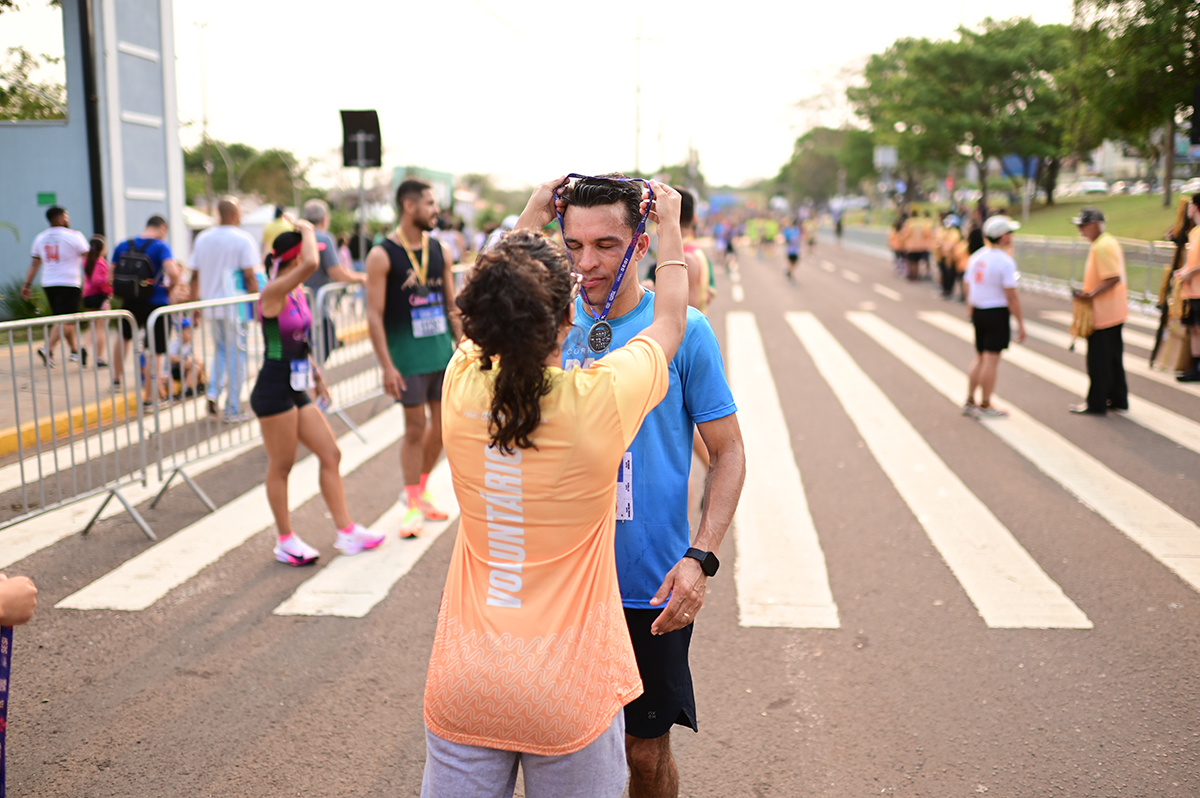 Corredor recebe medalha de participação entregue por voluntária da organização do evento