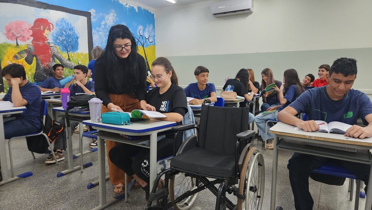 Jhennyfer na carteira escolar e junta à professora de apoio. - (Foto: Ricardo Agra/SED)