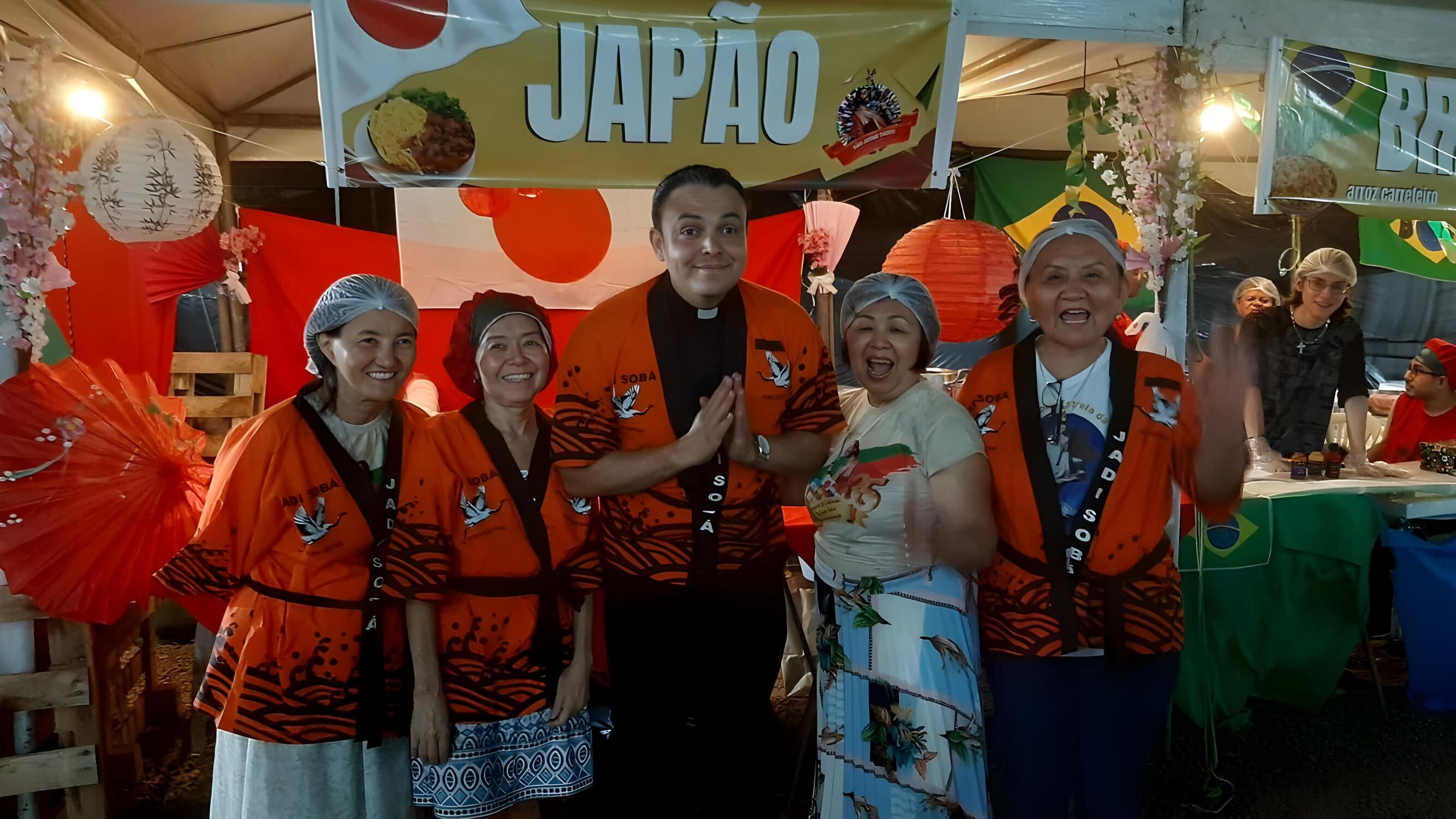 Equipe da barraca do Japão posa com o padre do Santuário durante a Festa das Nações, que celebra a cultura e a fé.