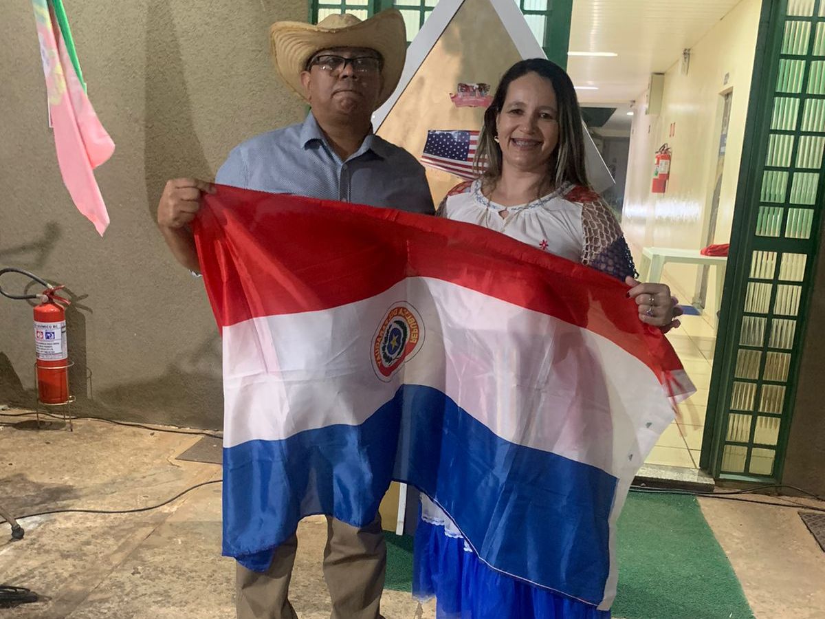 Casal representa o Paraguai na Festa das Nações do Santuário São Judas Tadeu, com trajes típicos e a bandeira do país.