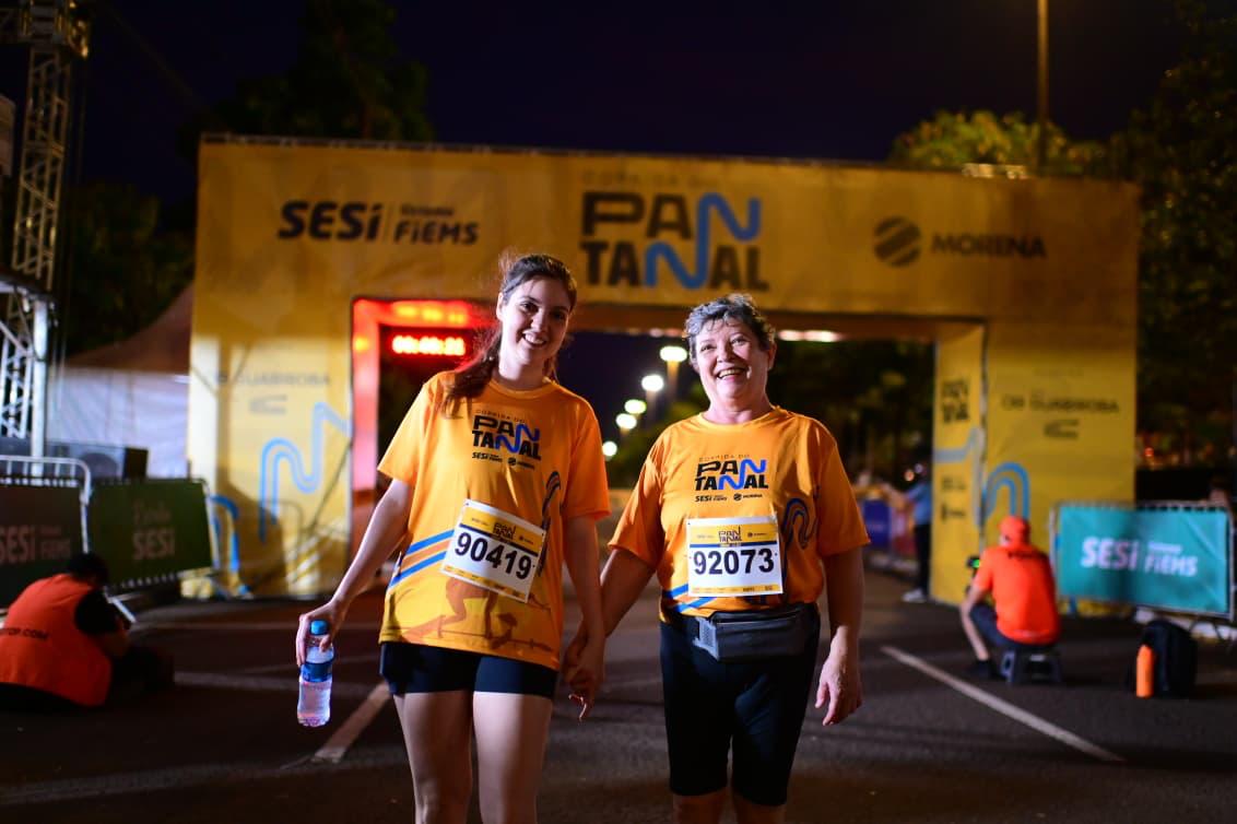 Mãe e filha cruzam sorrindo a linha de chegada da caminhada da Corrida do Pantanal 2025, em Campo Grande. (Foto: Divulgação)