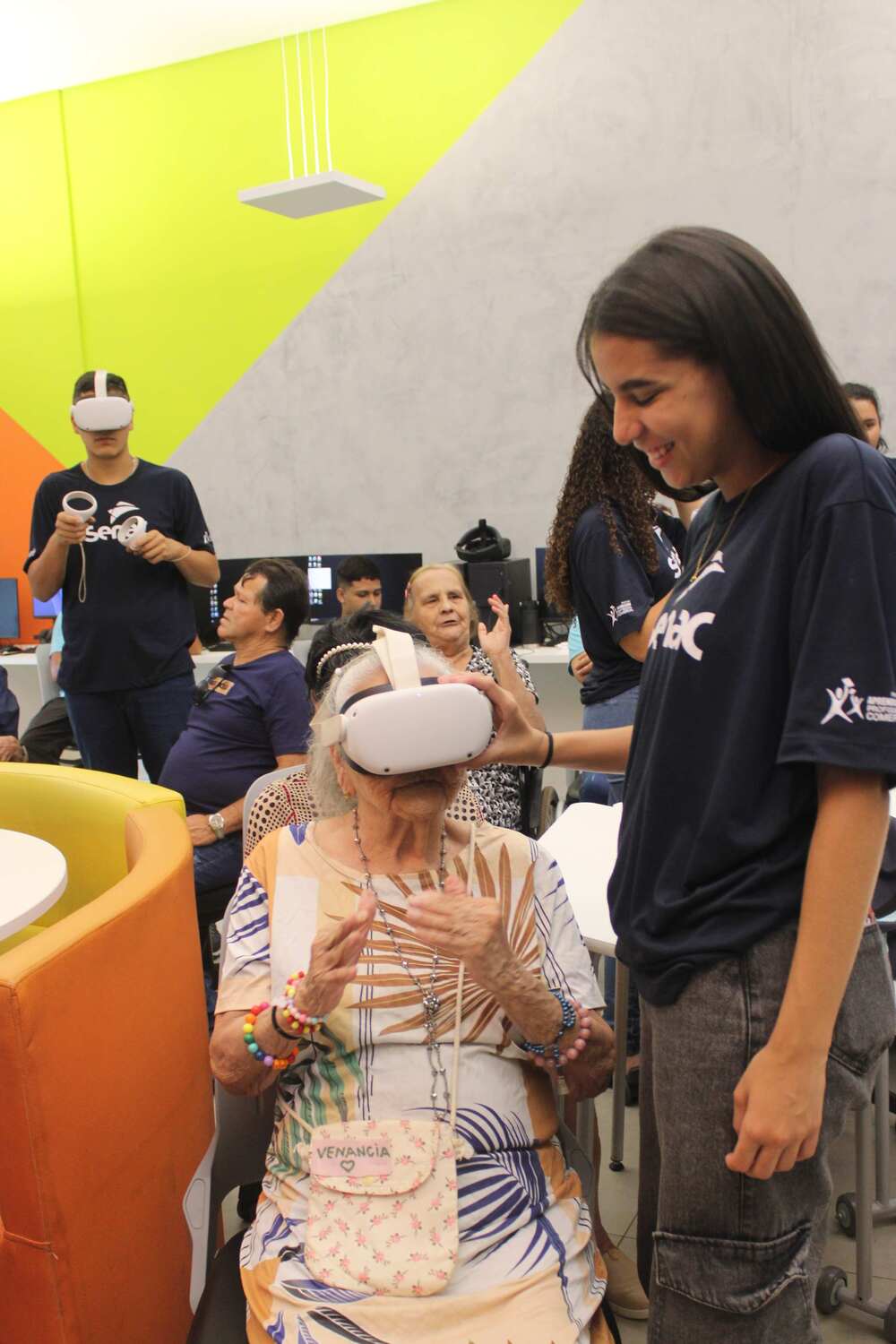 Moradora do Asilo São João Bosco experimenta óculos de realidade virtual durante visita ao Senac Hub Academy, em Campo Grande (MS).