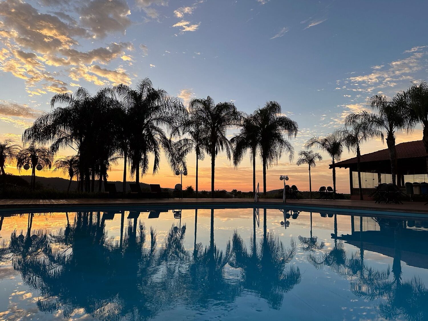 Piscina do Hotel Sesc Bonito em fim de tarde, com coqueiros refletidos na água e vista para o pôr do sol em Bonito (MS).