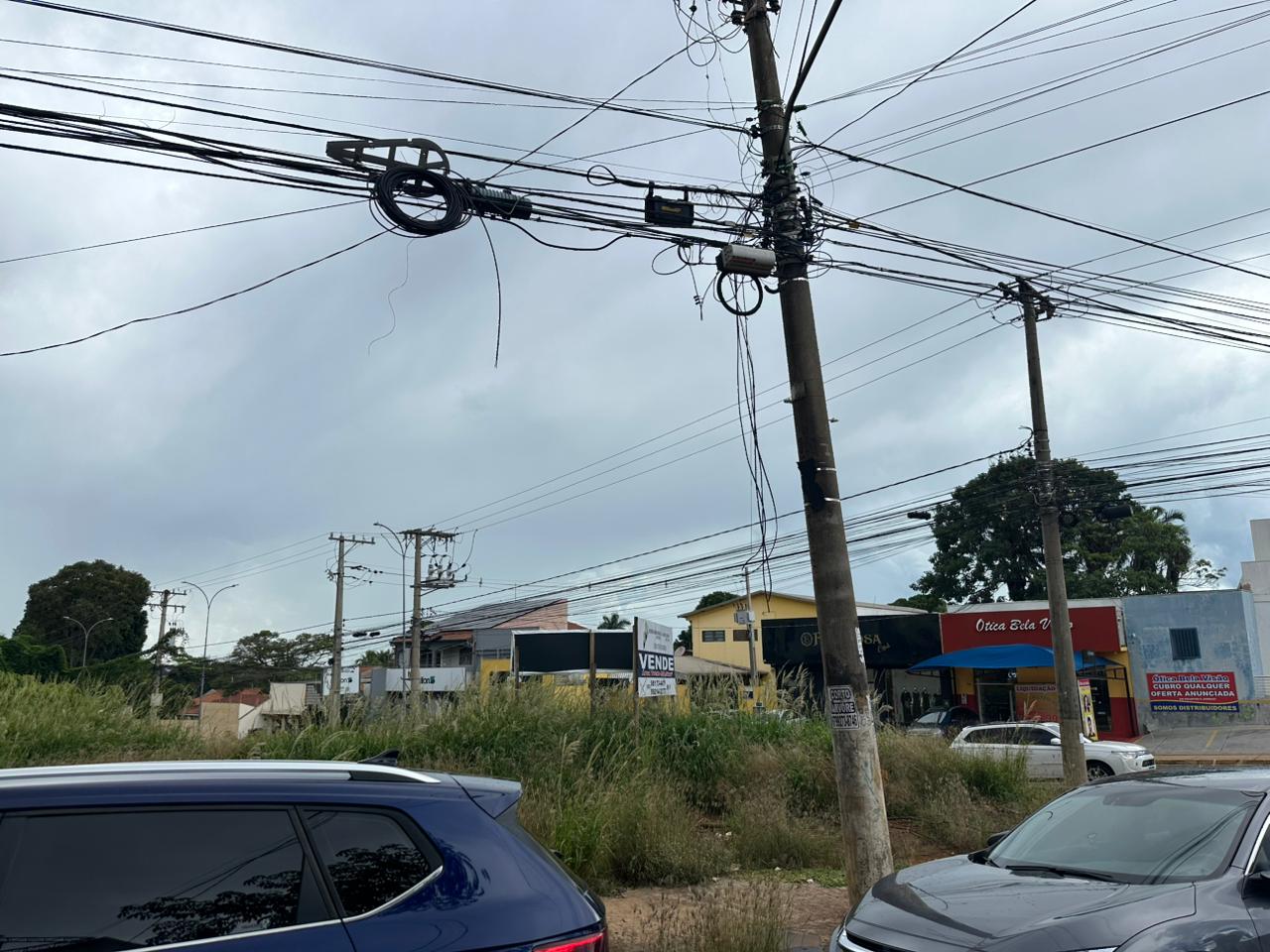 Fios de telefonia e internet pendurados em poste de Campo Grande seguem oferecendo risco a quem passa, mesmo após lei que obriga retirada de cabos inativos.